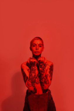 Dövme ve piercing. Dövmeleri olan, elleri göğüslerini kapatan ve kameraya bakan, üzerinde piercing olan beyaz bir kadın.