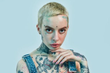 Dövme ve piercing. Yüzüne piercing takmış, başı hafifçe eğilmiş ve kameraya bakan beyaz dövmeli bir kadın.