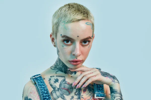 Tatuaje y piercing. Un primer plano de una mujer blanca tatuada con piercing con la palma de la mano cerca de la cara con la cabeza ligeramente inclinada y mirando a una cámara — Foto de Stock