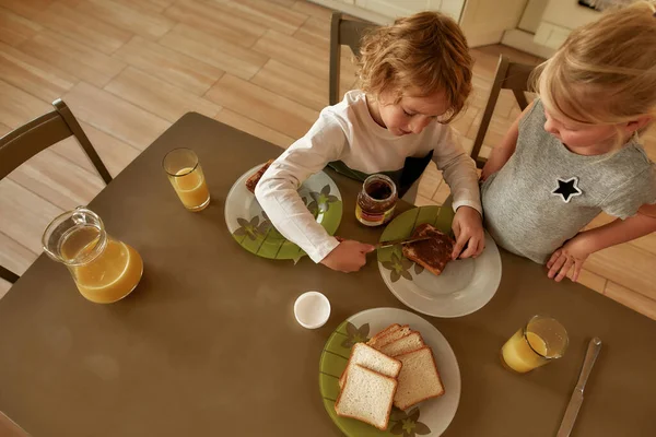 Mutfakta kahvaltı hazırlayan iki küçük çocuğun en iyi görüntüsü. Tatlı kardeşim kızarmış ekmeğe çikolata yağı sürüyor. — Stok fotoğraf