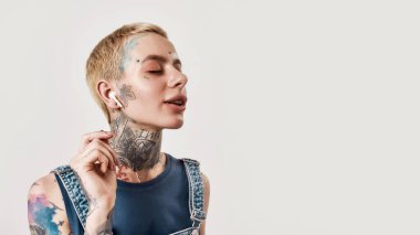 Müzik dinliyordum. Üzerinde piercing olan beyaz bir kızın portresi ayakta duran ve müzik dinleyen kablosuz kulaklıkları ve gözleri kapalı ve ağzı hafifçe açılmış bir kot pantolon giymiş.