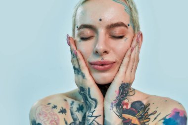 Dövme ve piercing. Gözü kapalı ve avuç içleri yanaklarında beyaz dövmeli bir kadın.