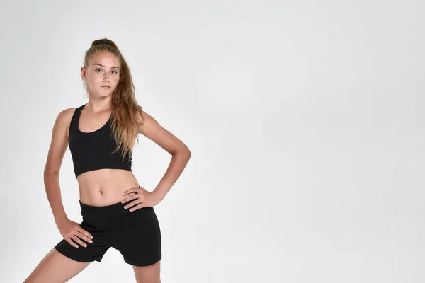 Porträt eines niedlichen sportlichen Mädchens in schwarzer Sportbekleidung, das in die Kamera blickt, während es isoliert auf weißem Hintergrund posiert — Stockfoto