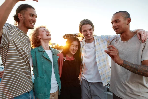 A group of young well-dressed friends of different nationalities hugging each other having a good time together outside laughing and smiling