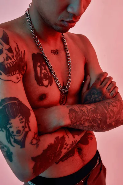 Tatouages apparaissant. Un corps tatoué d'un homme à la peau foncée debout seins nus, les mains croisées sur la poitrine, portant une chaîne à maillons grossiers — Photo