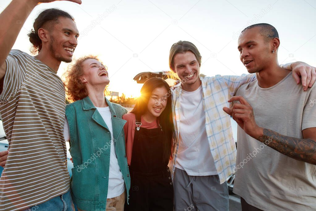 A group of young well-dressed friends of different nationalities hugging each other having a good time together outside laughing and smiling