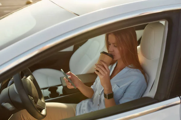 Mooie jonge vrouw kijkt in de telefoon zittend in de auto — Stockfoto