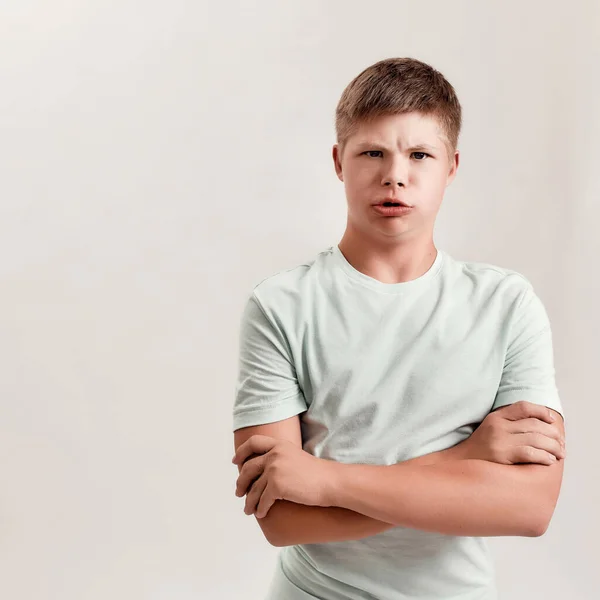 Retrato de un adolescente discapacitado con síndrome de Down haciendo caras graciosas, mirando gruñón a la cámara mientras posando aislado sobre fondo blanco — Foto de Stock