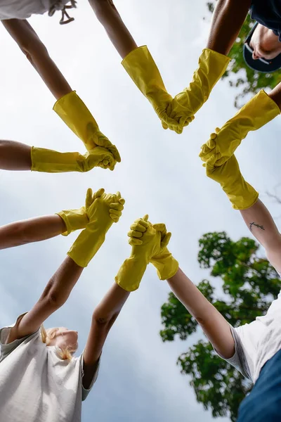 Gran trabajo en equipo. Foto vertical de eco activistas o voluntarios que usan guantes de goma de protección amarilla tomados de la mano, vista inferior —  Fotos de Stock