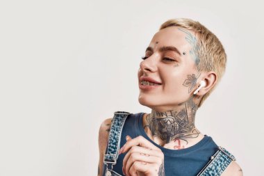 Müzik dinliyordum. Üzerinde kot pantolon olan, kablosuz kulaklıkları ve gözleri kapalı müzik dinlemekten zevk alan dövmeleri olan beyaz bir kızın portresi.
