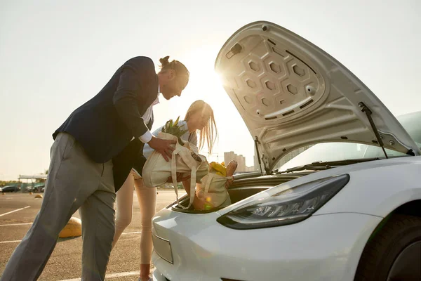 Joven hombre y mujer poniendo bolsas en la capucha del coche — Foto de Stock