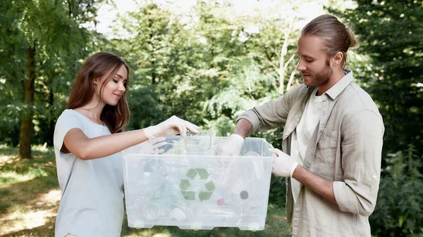 森や公園でプラスチック廃棄物を収集し、リサイクルビンを保持する若い美しいカップル — ストック写真