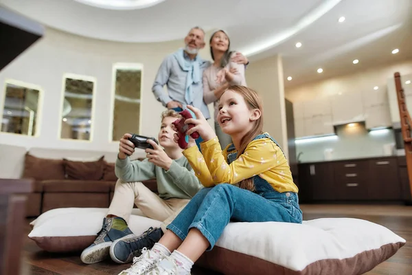 Nette kleine Jungen und Mädchen haben Spaß zu Hause, spielen Videospiele, während sie auf dem Boden sitzen, verbringen Zeit mit den Großeltern — Stockfoto