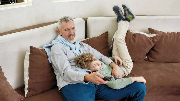 Aile zamanı. Mutlu bir büyükbabanın portresi ve heyecanlı bir torunun kucaklaşması, eğlenmesi ve evdeki bir kanepede dinlenmesi. — Stok fotoğraf