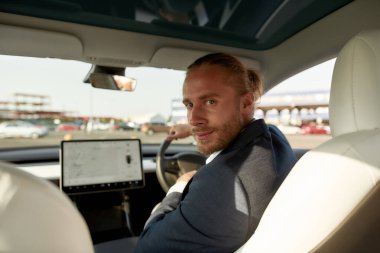 Kafkasyalı genç adam geriye dönüp araba kuaförüne bakıyor.