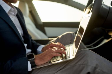 Dizüstü bilgisayarlı bir adam sürücü koltuğunda oturuyor.