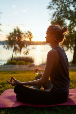 Spor kıyafetleri giyen, yoga yapan, nilüfer çiçekli poz verip meditasyon yapan genç bir kadının yan görüntüsü.