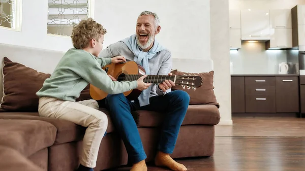 おじいちゃんと週末。陽気な大人の男、祖父は彼のかわいい小さな孫にギターを演奏 — ストック写真