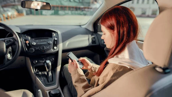 Portret van een tienermeisje dat glimlacht naar het scherm terwijl ze haar telefoon gebruikt, zittend in de auto. Zicht vanaf de achterbank — Stockfoto