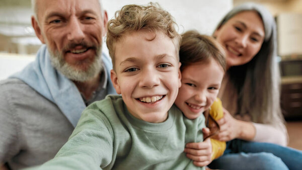 Having fun at home. Two excited kids, boy and girl making a selfie with grandparent, playing and spending great time together