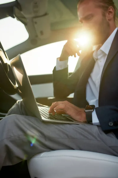 Laptop in hands of young working businessman in car