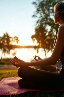 Derin bir rahatlama. Bir kadının sabah dışarıda yoga yaparken, nilüfer çiçeğinin arkasında otururken ve meditasyon yaparken dikey çekimi.