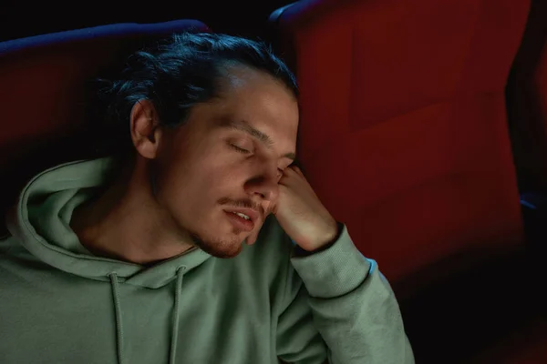 Portrait of young man falling asleep in chair while watching a movie at the cinema