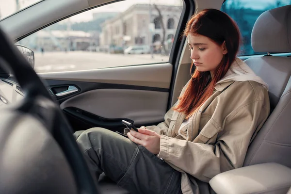 Έφηβο κορίτσι που δείχνει να βαριέται ενώ χρησιμοποιεί το τηλέφωνό της, κάθεται στο αυτοκίνητο. Έννοια εξάρτησης από smartphone — Φωτογραφία Αρχείου