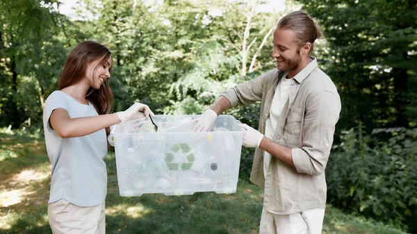 Eco friendly. Young beautiful couple holding recycle bin, collecting plastic waste in the forest or park — Stock Photo, Image