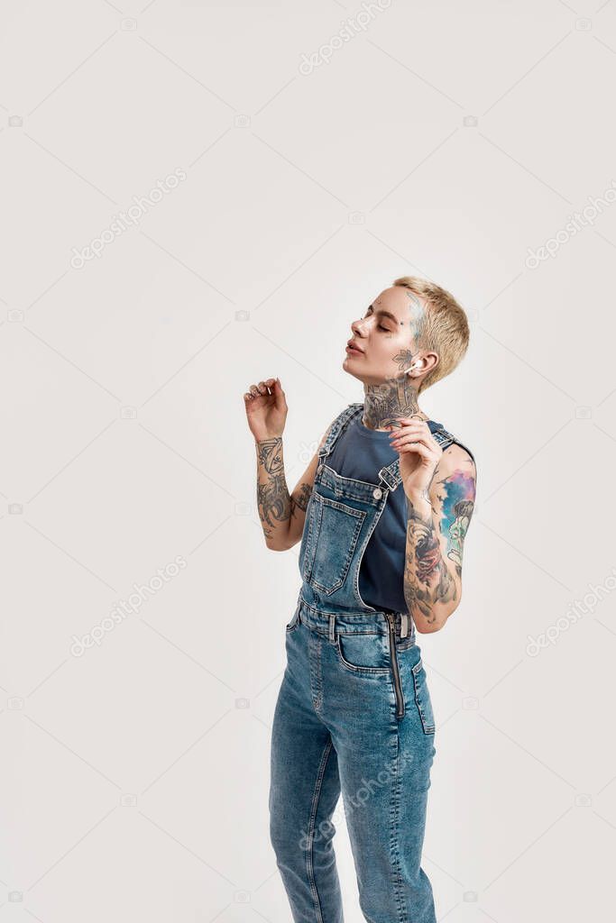 Listening to music. A white tattooed pierced girl wearing denim overall listening and dancing to music with her wireless earphones eyes closed and smiling