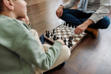Küçük düşünceli çocuk evde oturma odasında yerde otururken büyükbabasıyla satranç oynuyor.