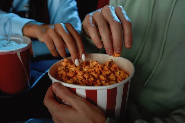 Nahaufnahme der Hände eines Mädchens und eines Mannes, die Popcorn aus dem Korb holen, während sie gemeinsam einen Film im Kino ansehen — Stockfoto