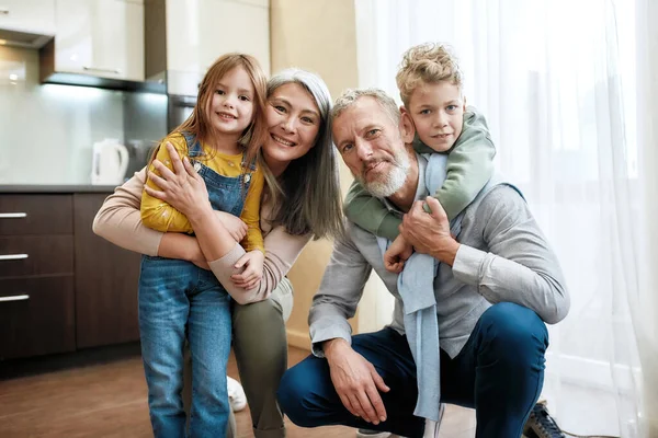 Porträt einer fröhlichen Familie, Großeltern mit Enkeln, die Zeit zu Hause verbringen, in die Kamera schauen und in der Küche lächeln — Stockfoto