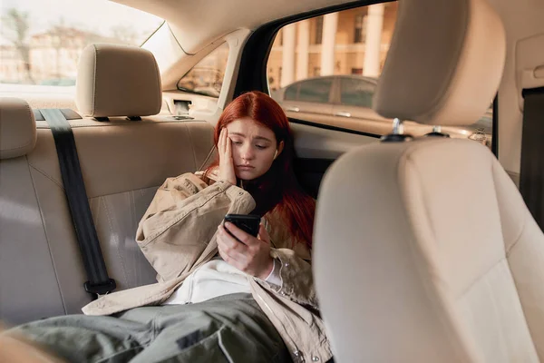 Έφηβη κοπέλα με ακουστικά που δείχνει συναισθηματική, βλέποντας βίντεο χρησιμοποιώντας το smartphone της, ενώ κάθεται στο πίσω κάθισμα του αυτοκινήτου — Φωτογραφία Αρχείου