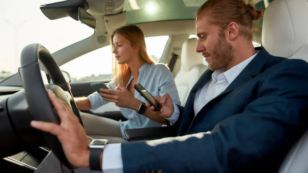 Jovem casal caucasiano segurando smartphones dentro do carro — Fotografia de Stock