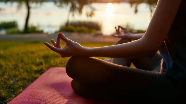 Entspannungsübungen. Schnappschuss einer Frau, die morgens im Freien Yoga praktiziert, in Lotus-Pose sitzt und im Park am See meditiert, selektiver Fokus — Stockfoto