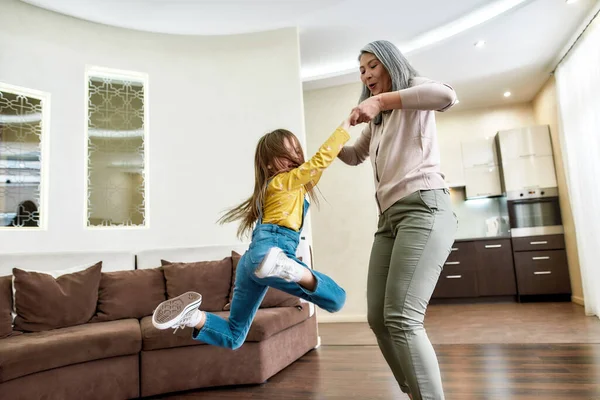 Essere nonna e 'divertente. Felice nonna giocare con la sua adorabile nipotina, sollevandola in aria mentre si diverte insieme in un soggiorno a casa — Foto Stock