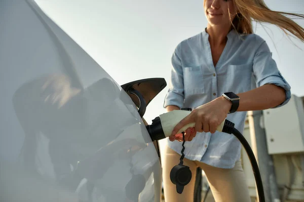 Mujer enchufando el cable eléctrico en el vehículo para cargar — Foto de Stock