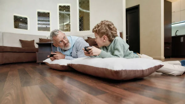 祖父と孫と枕の上に床に横たわってビデオゲームをプレイ,家で一緒に時間を過ごす — ストック写真