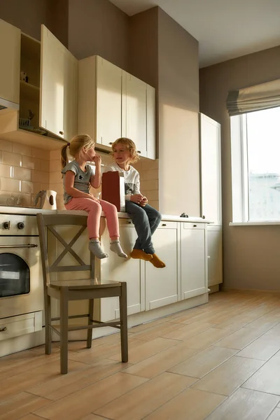 Портрет двох радісних дітей, брат і сестра їдять кукурудзяні пластівці, сидячи разом на кухонному шафі вдома — стокове фото