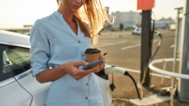 Araba şarj olmayı beklerken telefonu kaydıran kadın