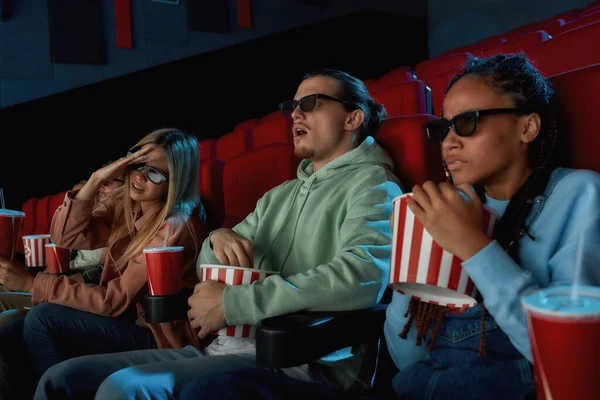 Группа молодых друзей в очках, пьющих попкорн во время просмотра фильма вместе в кинозале — стоковое фото