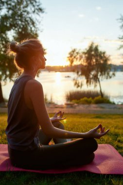 Spor kıyafetleri giyen, yoga yapan, nilüfer çiçekli poz veren ve doğanın arka planında meditasyon yapan bir kadının yan görüntüsü.