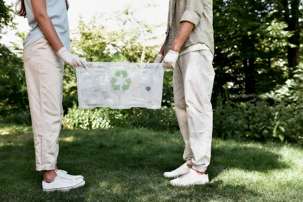 Salva nuestra naturaleza. Recorte de dos voluntarios sosteniendo la papelera de reciclaje con residuos de plástico mientras están de pie en el bosque o parque —  Fotos de Stock