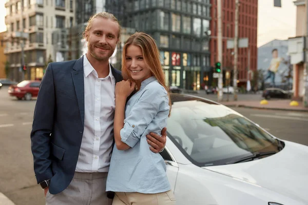 Vrolijke jonge Kaukasische zakenman knuffelen jong meisje in de buurt van auto — Stockfoto