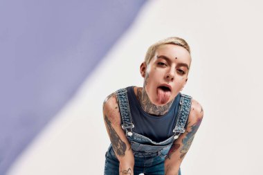 Dövme ve piercing. Piercing ve dövme yaptıran beyaz bir kadının dikilirken ve kot pantolon giyerken kameraya baktığı yakın plan bir fotoğraf.