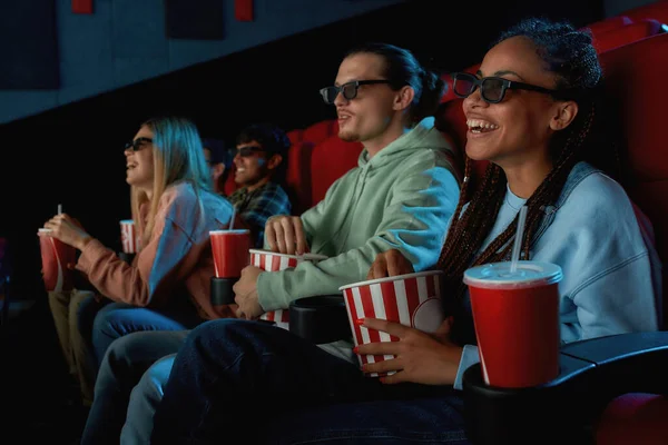 Fröhliche junge Frau mit Brille, die Popcorn isst, während sie mit ihrem Freund im Kinosaal einen Film anschaut — Stockfoto