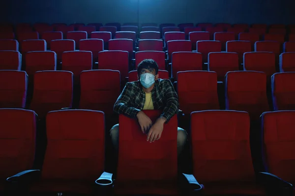 Volledige shot van jonge man in beschermende gezichtsmasker kijken naar een film, een bezoek aan de bioscoop alleen tijdens coronavirus pandemie — Stockfoto