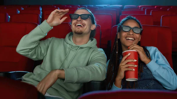 Портрет веселой молодой пары в трехмерных очках, улыбающейся во время просмотра фильма вместе в кинозале и питьевой содовой — стоковое фото