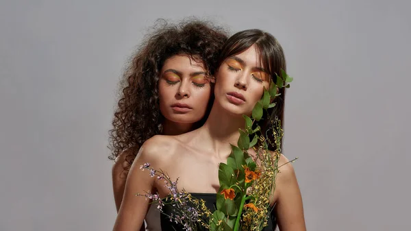 Mulheres desfrutando de seu abraço segurando uma composição de flores — Fotografia de Stock